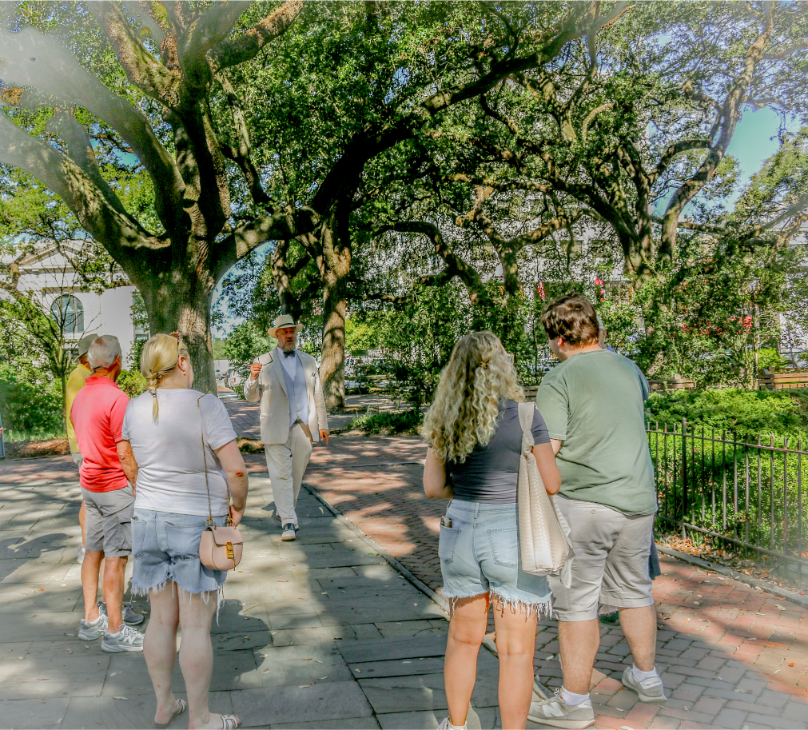 Tour guide leads group on scenic historic walking tour under large trees in sunny park setting