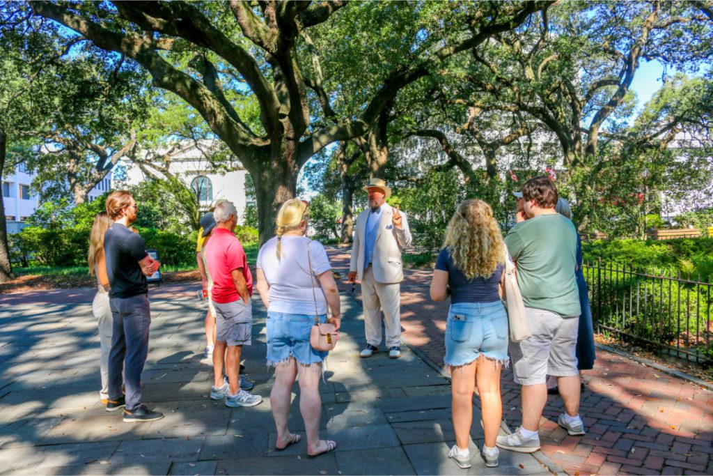 Tour guide leads a group under large trees in a park setting