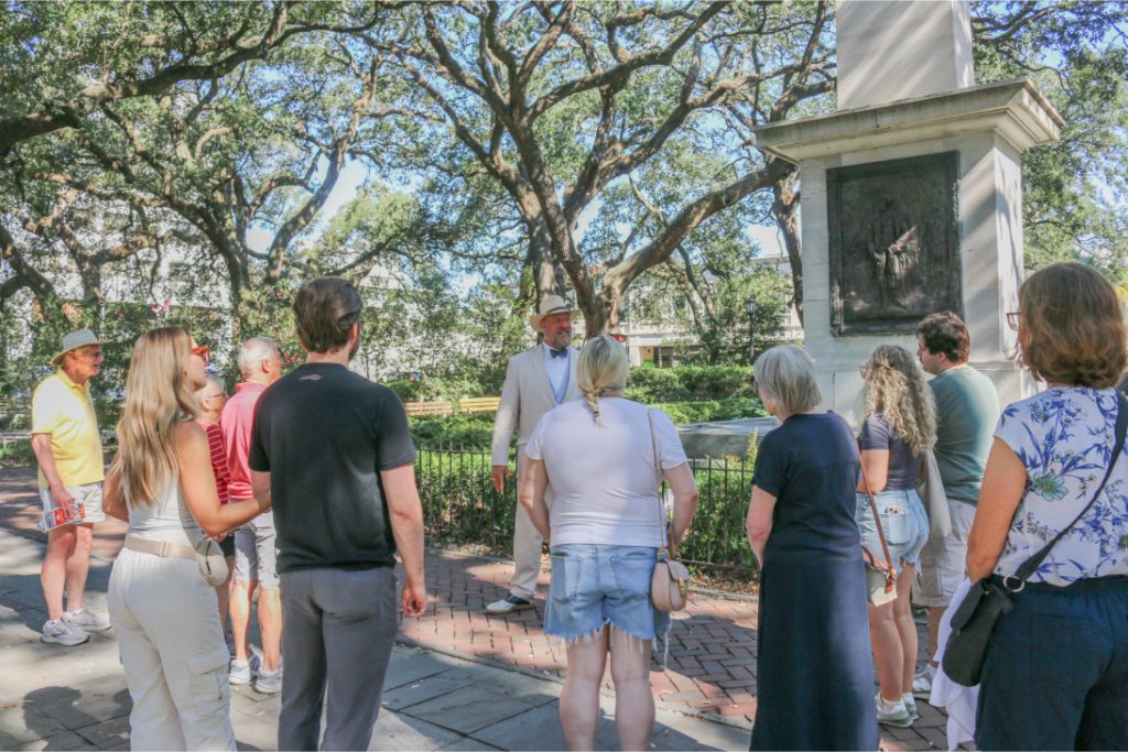 Group of tourists listening to a guide at a historic site under large trees