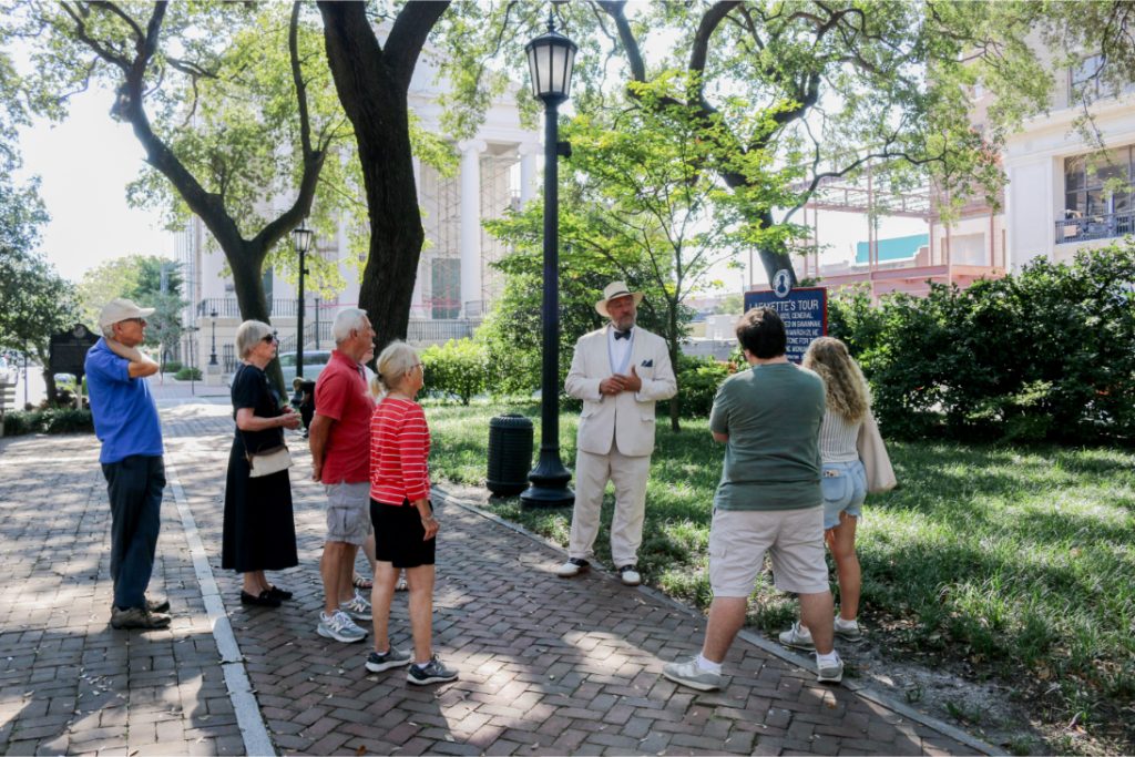 Group enjoying a guided walking tour in a park setting with historical buildings around