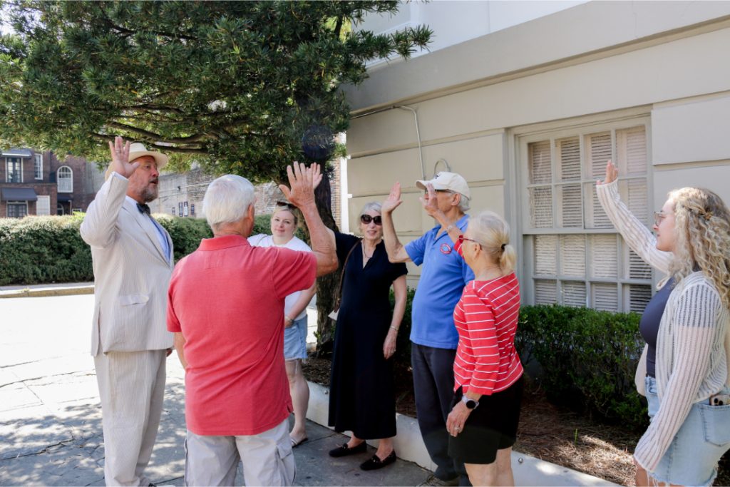 Group of people engaging in outdoor activity, high-fiving under a tree, wearing casual clothing, urban setting