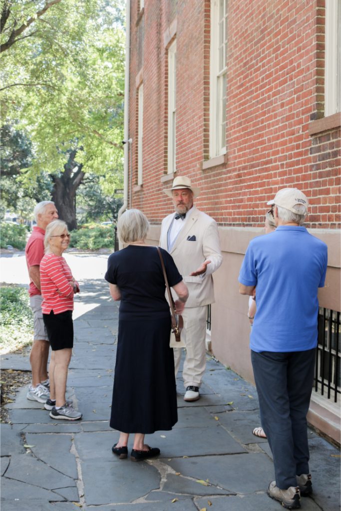 Group of adults on a guided walking tour near a historic brick building in a sunny park setting