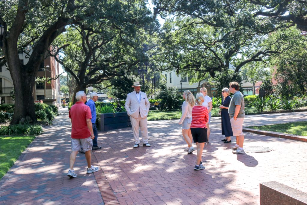A group of people on a guided walking tour in a sunny park with trees and brick pathways