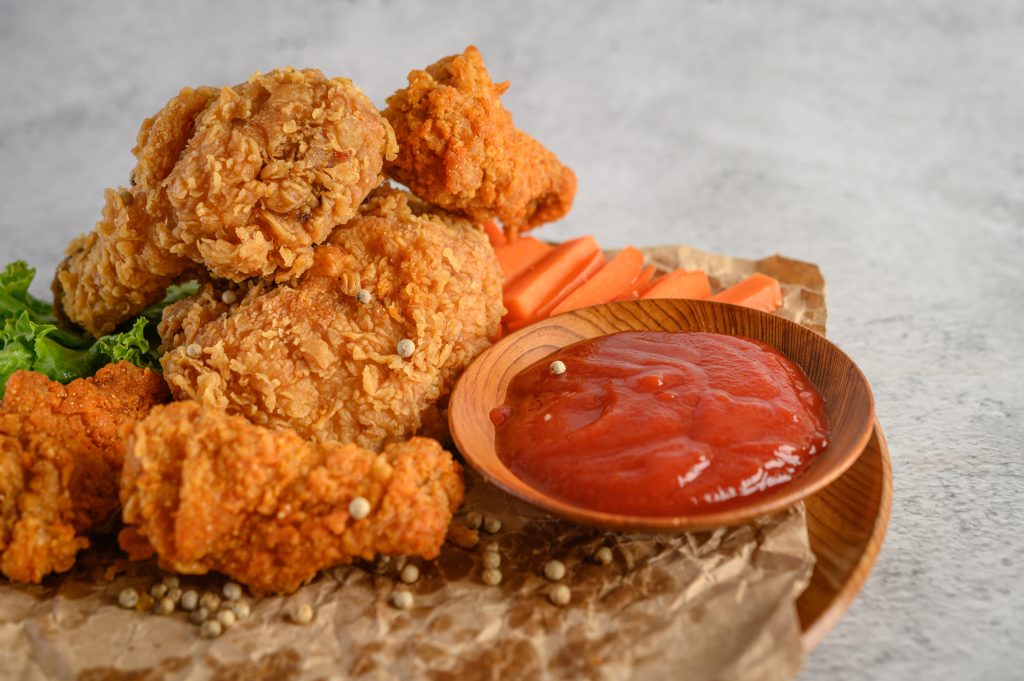 Crispy fried chicken with spicy sauce and fresh carrot sticks on a wooden plate, garnished with lettuce leaves