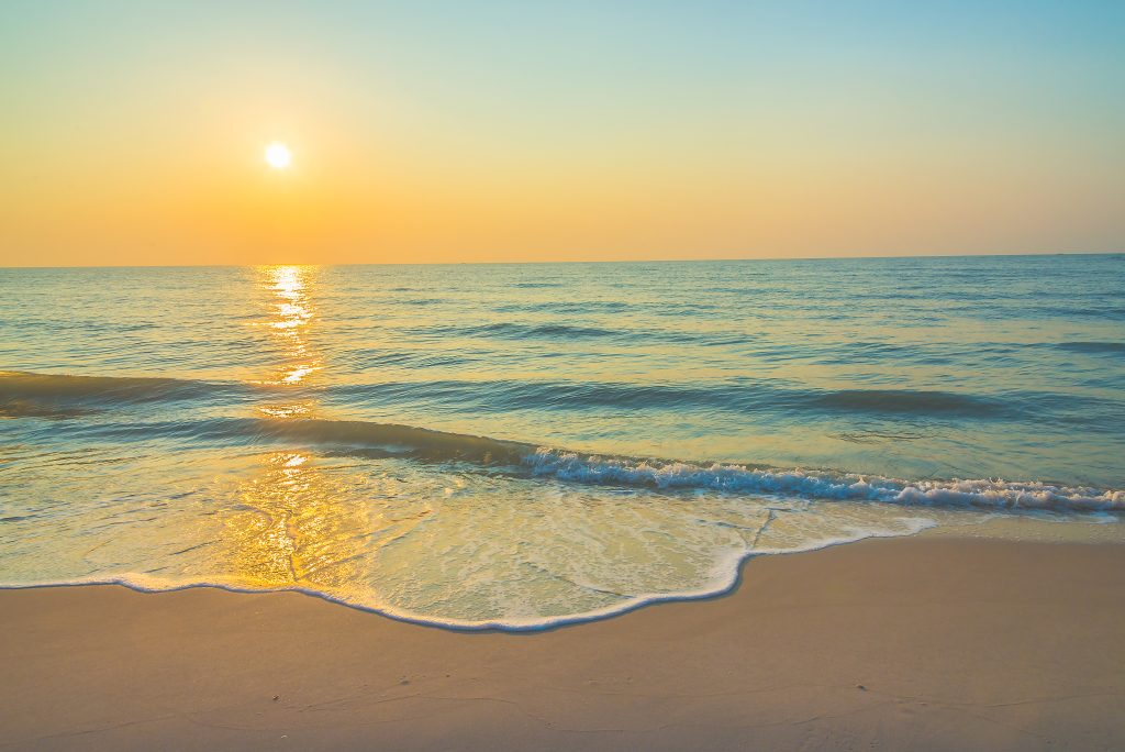 Sunset over a tranquil beach with gentle waves and a golden sky reflecting on the ocean water
