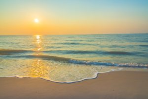 Sunset over a tranquil beach with gentle waves and a golden sky reflecting on the ocean water