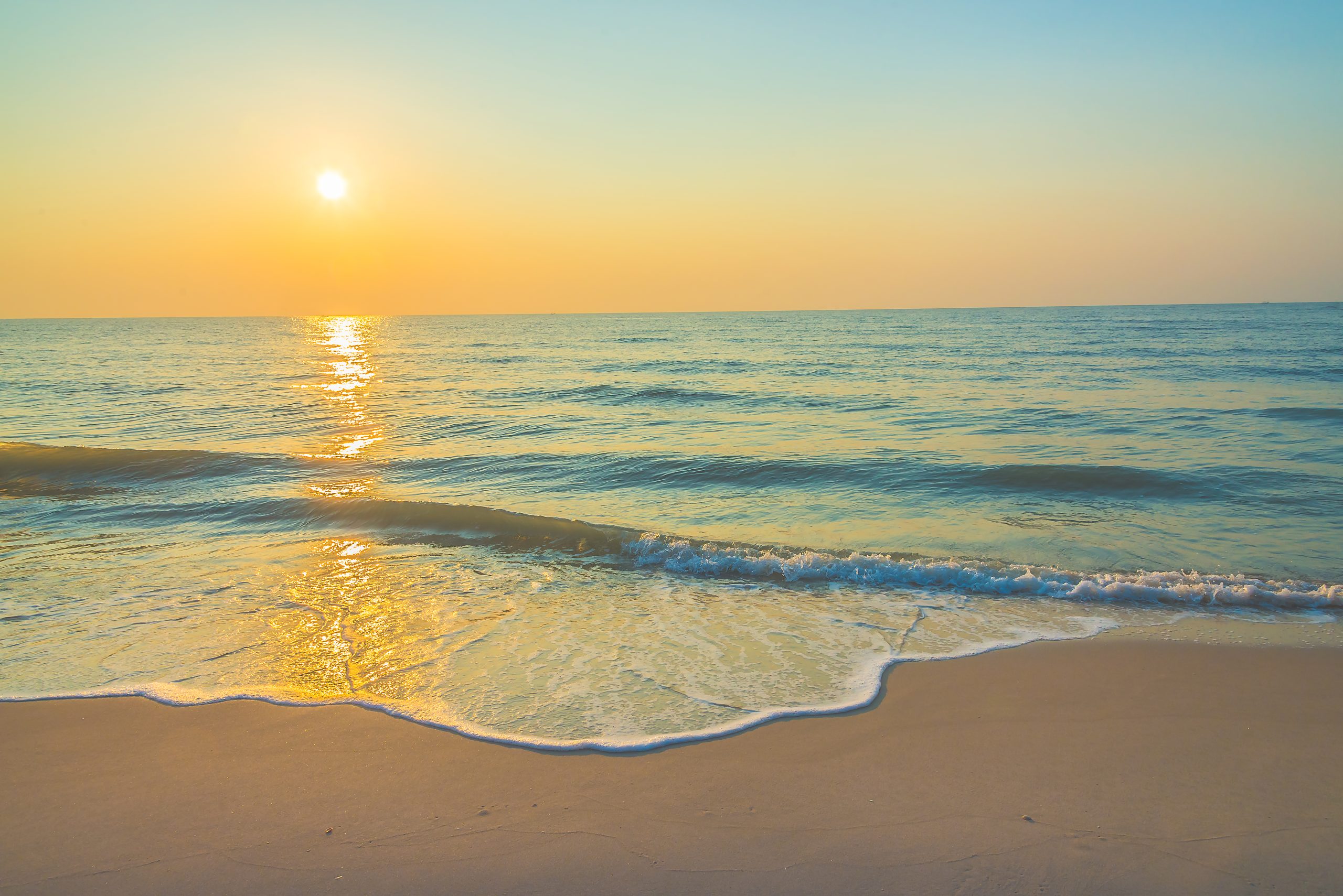 Sunset over a tranquil beach with gentle waves and a golden sky reflecting on the ocean water